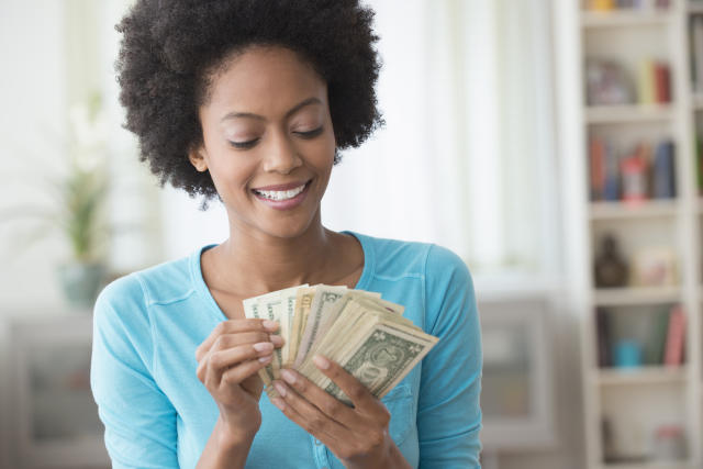 Smiling woman holding cash, symbolizing financial success and budgeting